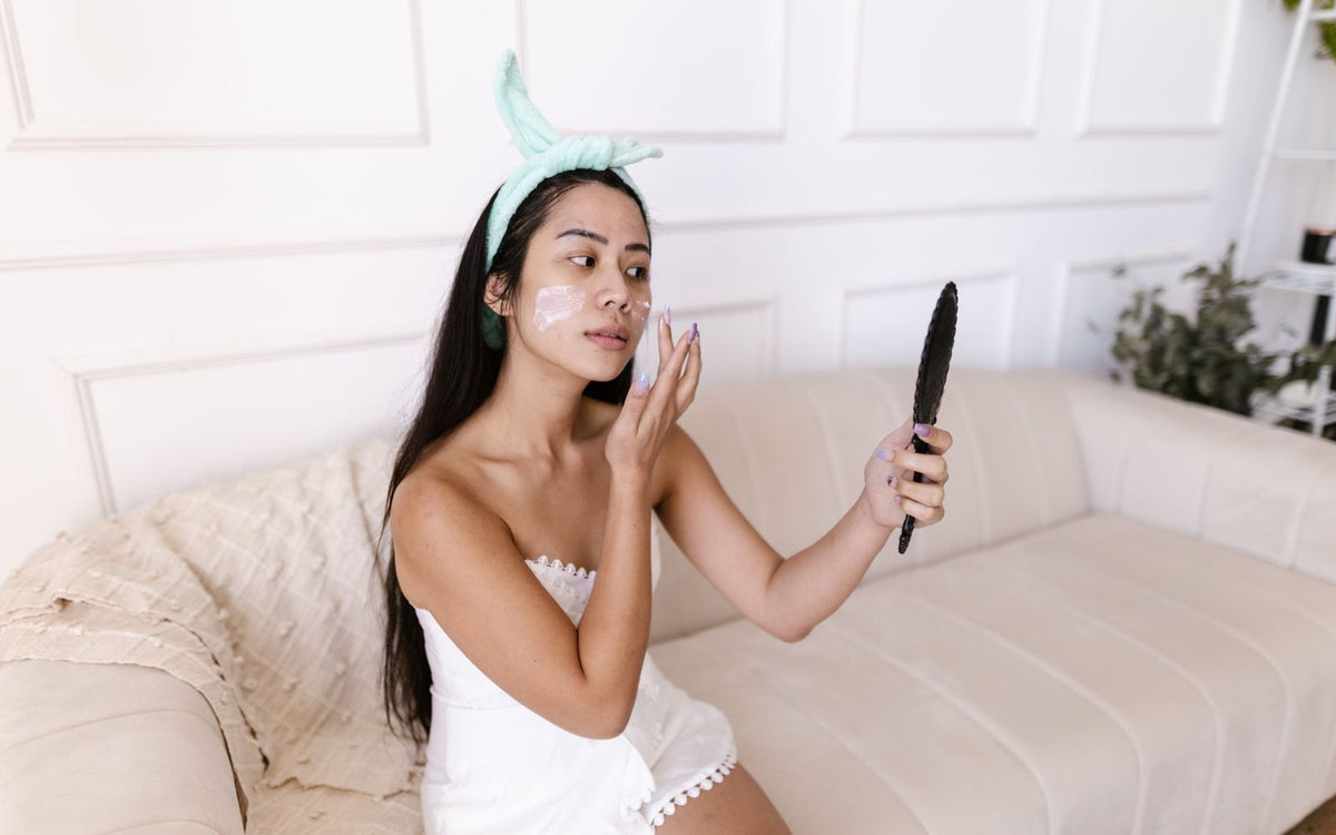 Asian woman with dull skin examining her face in soft light